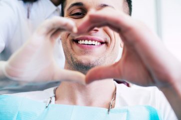 Cheer of heart. A patient with white and healthy smile in the center of a heart made from two hands of a doctor and a patient which is telling about pleasant emotions of the appointment.